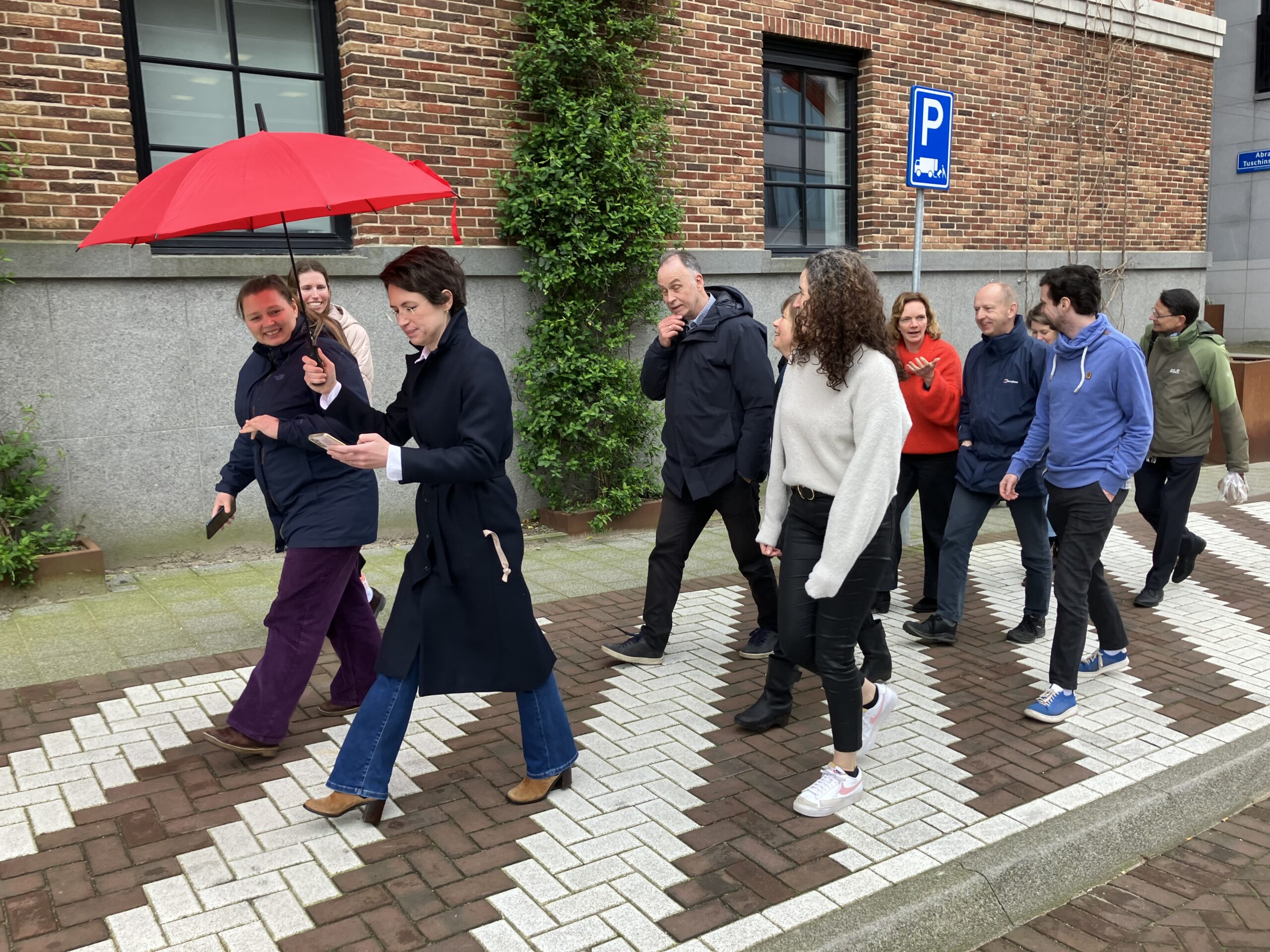 De medewerkers lopen langs Kleine C, met Marta voorop met de rode paraplu.