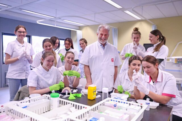 Foto van Wim omringd door studenten verpleegkunde in werkkleding