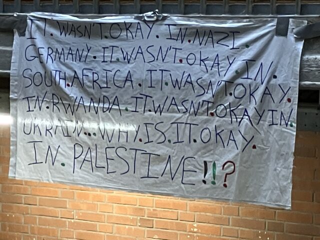 Het spandoek met de tekst: ‘It wasn’t okay in nazi-Germany. It wasn’t okay in South Africa. It wasn’t okay in Rwanda. It wasn’t okay in Ukrain… Why is it okay in Palestina!!?’