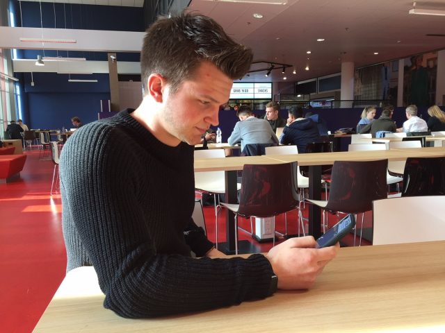 Max Brand in de kantine van locatie Kralingse Zoom kijkend naar zijn app op z'n telefoon.